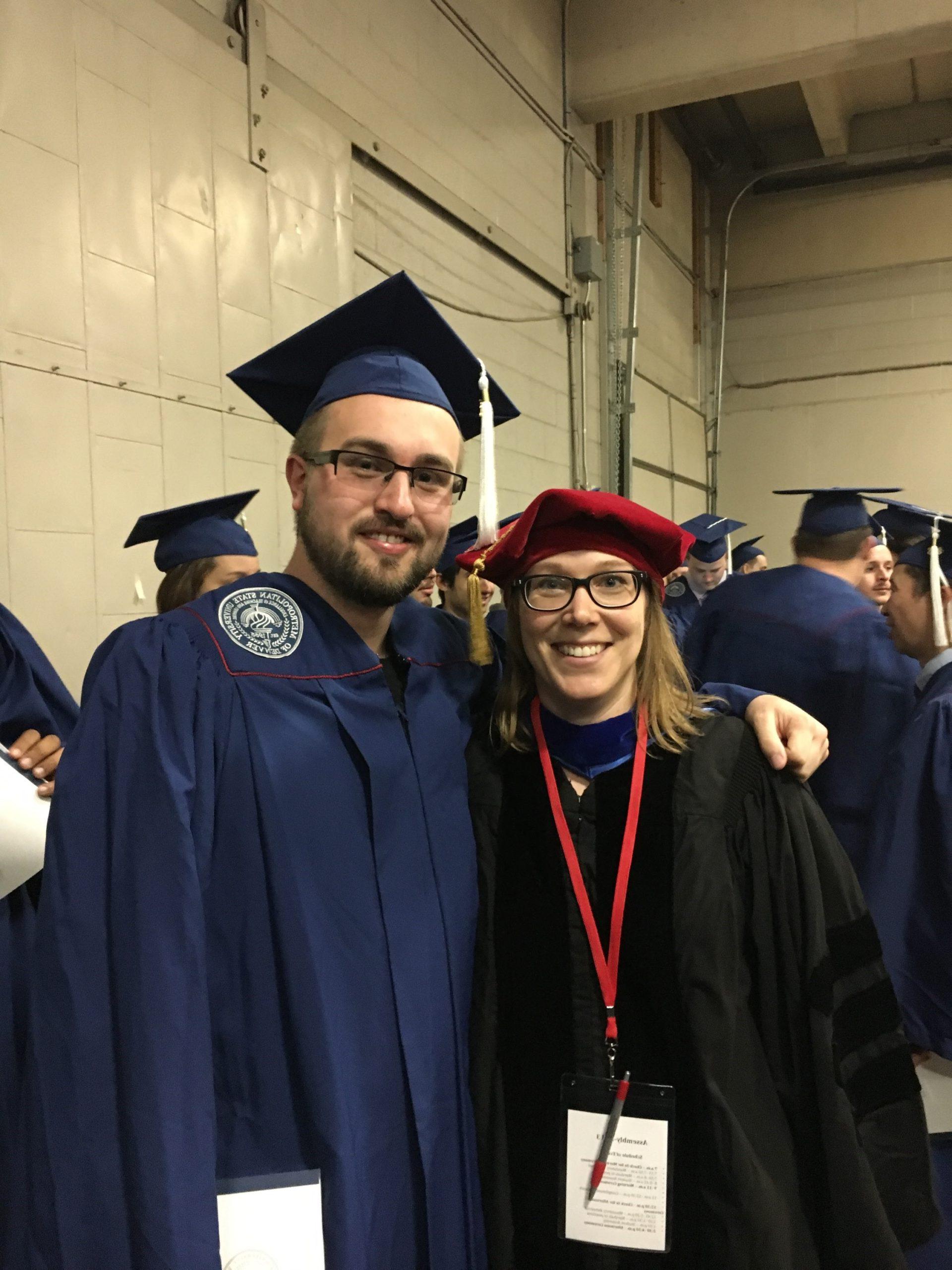 Cody Griffith in a cap and gown, posing with a professor