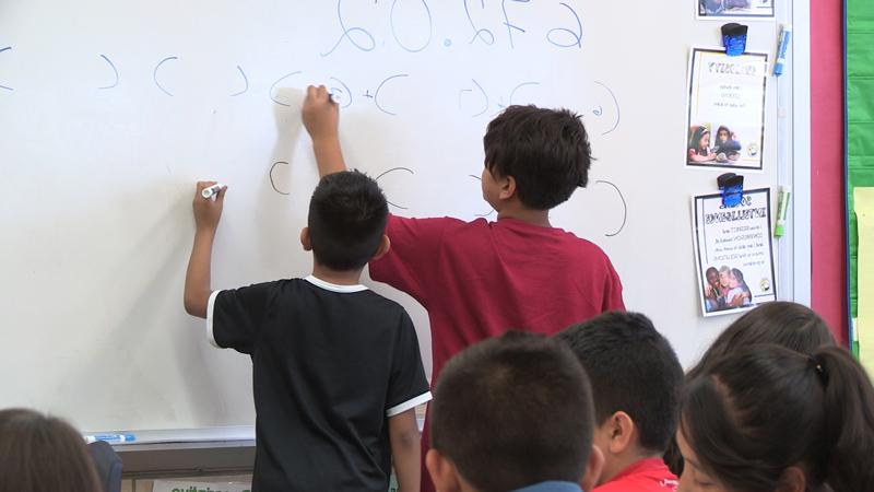 Image of two elementary school boys standing at the white board solving a math equation.