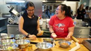 Sophia Tran and Stephanie Lee demonstrated how to make momos, a popular Nepalese dumpling, in a recent workshop in the School of Hospitality kitchen. Both are seen here laughing and cajoling, with a spread of dishes in front of them as they make the dumplings.