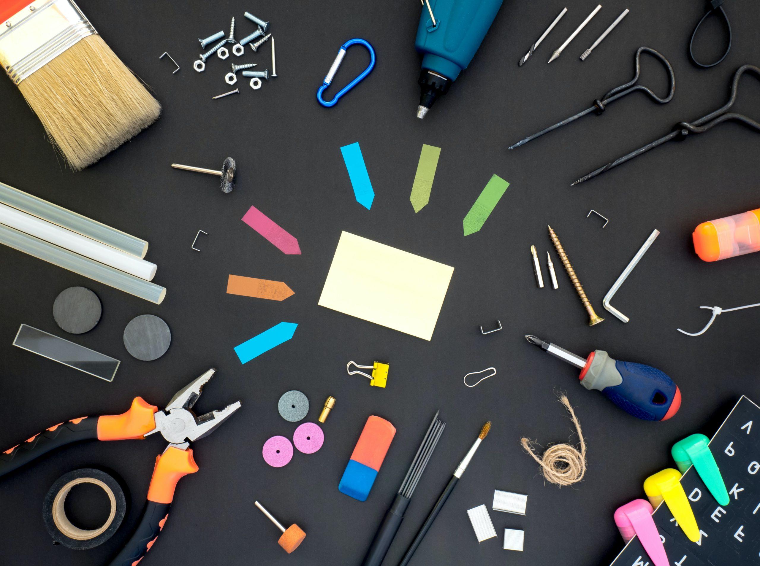 An assortment of tools laying on a black surface including post-its, 螺丝刀, 扳手, 磁带, 画笔, 笔用, 胶棒, 斯台普斯, 磁铁, 和回形针.