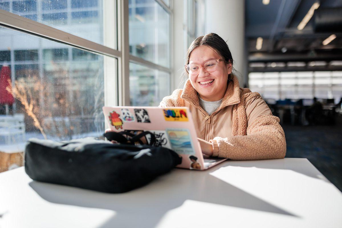 Latinx woman smiling at her computer in the Auraria Library
